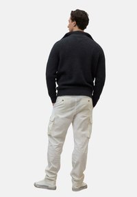 Ciemnoszara sweter dzianinowy z kołnierzem szalowym, połączony z jasnobeżowymi spodniami cargo z bocznymi kieszeniami i elastycznymi mankietami. Białe sneakersy.