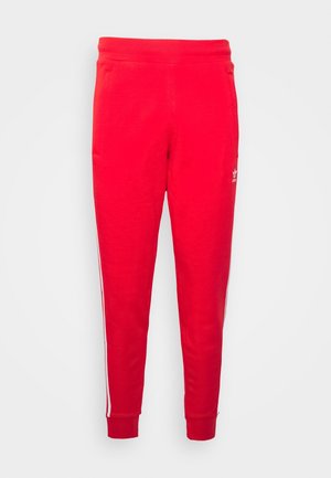 Czerwone spodnie dresowe Adidas z białymi paskami po bokach i elastycznymi ściągaczami, pokazane na jednolitym tle.