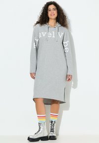 Harmaa hupparimekko rennolla istuvuudella, jossa valkoiset tekstit hihoissa, sivuhalkiot, yhdistetty hopeisiin nauhallisiin saappaisiin ja raidallisiin sukkahousuihin.