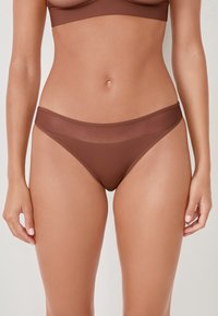 Parte inferiore di bikini marrone realizzata in un tessuto morbido ed elastico. Presenta un design semplice con una fascia media in vita e copertura minima.