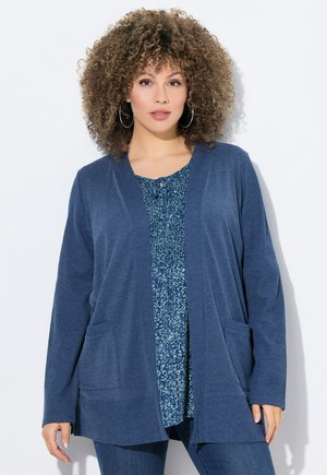 Cardigan bleu marine en tissu texturé, doté d'une ouverture sur le devant, de deux poches avant et porté sur un chemisier �à motif floral.