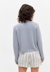 Ljusblå stickad tröja med rund halsringning, ribbade kanter och avslappnad passform, kombinerad med randiga, texturerade shorts.