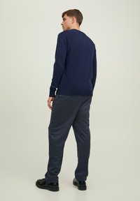 Granatowy sweter dzianinowy z okrągłym dekoltem, ściągaczami przy mankietach i u dołu, zestawiony z luźnymi, ciemnoszarymi spodniami i czarnymi butami, widok z tyłu.