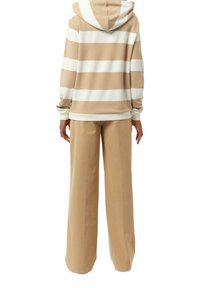 Sudadera con capucha a rayas beige y blancas, de mangas largas, combinada con pantalones anchos beige, que presentan un diseño relajado y una textura suave.