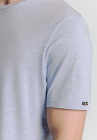Lichtblauwe T-shirt met korte mouwen, gemaakt van zachte stof, met een ronde halslijn en een klein zwart hardwaredetail op de mouw.