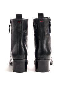 Paire de bottines noires en cuir avec talons carrés et fermetures éclair à l'arrière, vues de dos sur fond blanc.