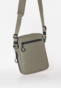 Khaki schoudertas met een gewatteerde textuur. Heeft een voorzak met rits en een verstelbare strap met zwarte hardware accenten.
