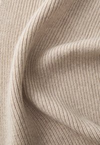 Beige ribbestrikket stoff med myk tekstur, med tydelige vertikale linjer og subtile variasjoner i fargetoner.
