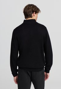 Maglione nero lavorato a maglia con colletto alto, polsini e orlo a coste. Il design presenta una superficie testurizzata e una vestibilità comoda.