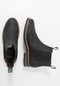 Botas Chelsea de couro preto com painéis laterais elásticos, costura de destaque castanha e sola texturizada. Etiqueta de marca verde no calcanhar.