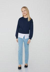 Námořnická mikina přes bílou košili s knoflíky, v kombinaci se světle modrými džíny a černými balerínami. Oblečení má ležérní vrstvený vzhled.