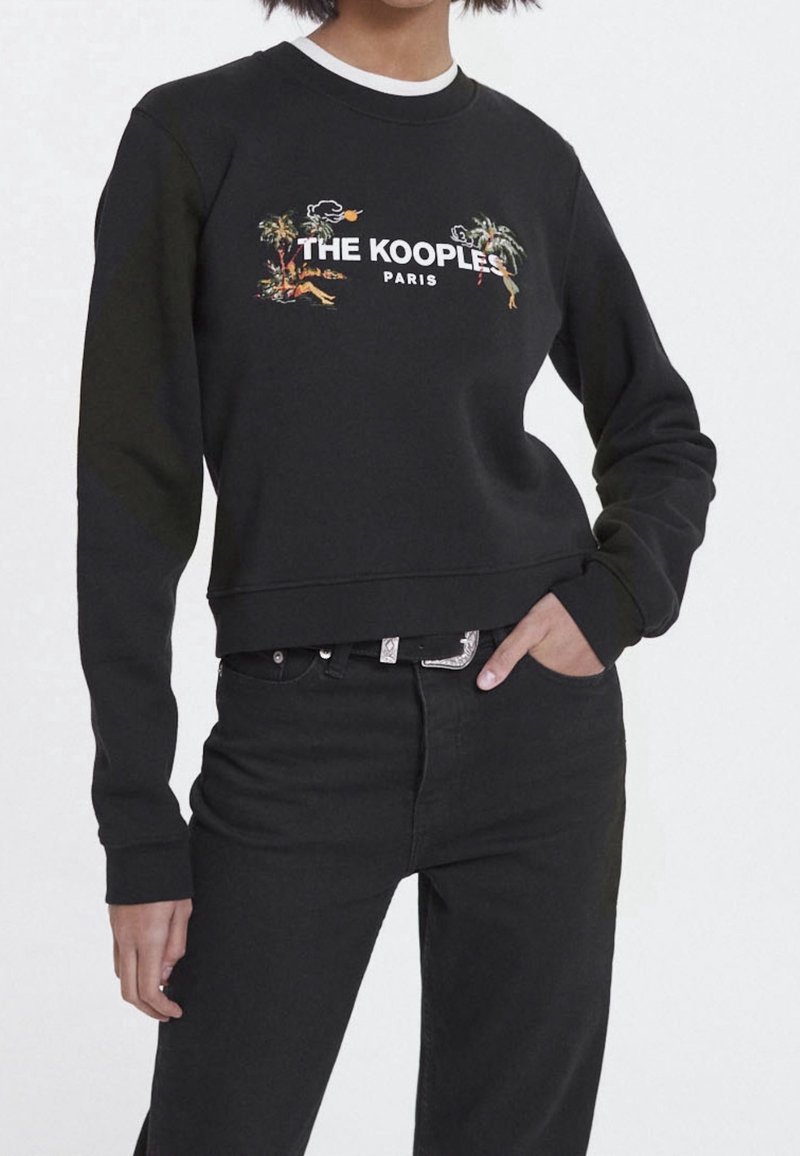 Černá mikina vyrobená z měkkého materiálu, s barevným tropickým potiskem a logem "THE KOOPLE" na přední straně. Krátký design s dlouhými rukávy.