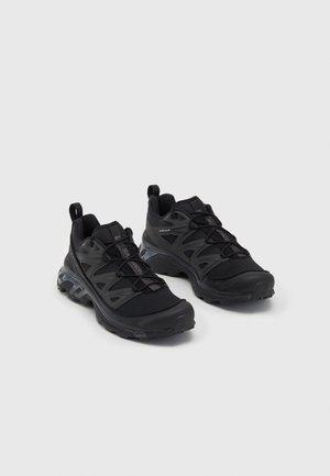 Black athletic shoes featuring a mesh upper, flexible design, textured sole, and pronounced lacing system with pull tabs for easy wear.