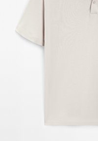 Beige polo skjorta med korta ärmar, med en placket med två knappar och mjuk textur. Diskret glans och jämna sömmar längs fållen.