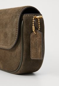 Brown suede handbag with rounded shape, dark leather trim, gold-toned hardware, and a detachable tag featuring “COACH” branding.