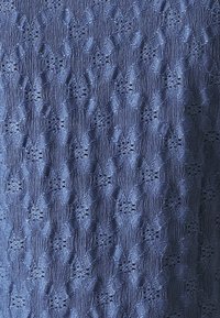 Námořnická texturovaná látka s vzorovaným designem obsahujícím vyvýšené diamantové tvary a malé výřezy, které vytvářejí rytmický vizuální efekt.