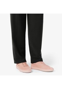 Sneakers texturizzati rosa chiaro con profilo basso, caratterizzati da una suola piatta e design con lacci, abbinati a pantaloni a scacchi neri.