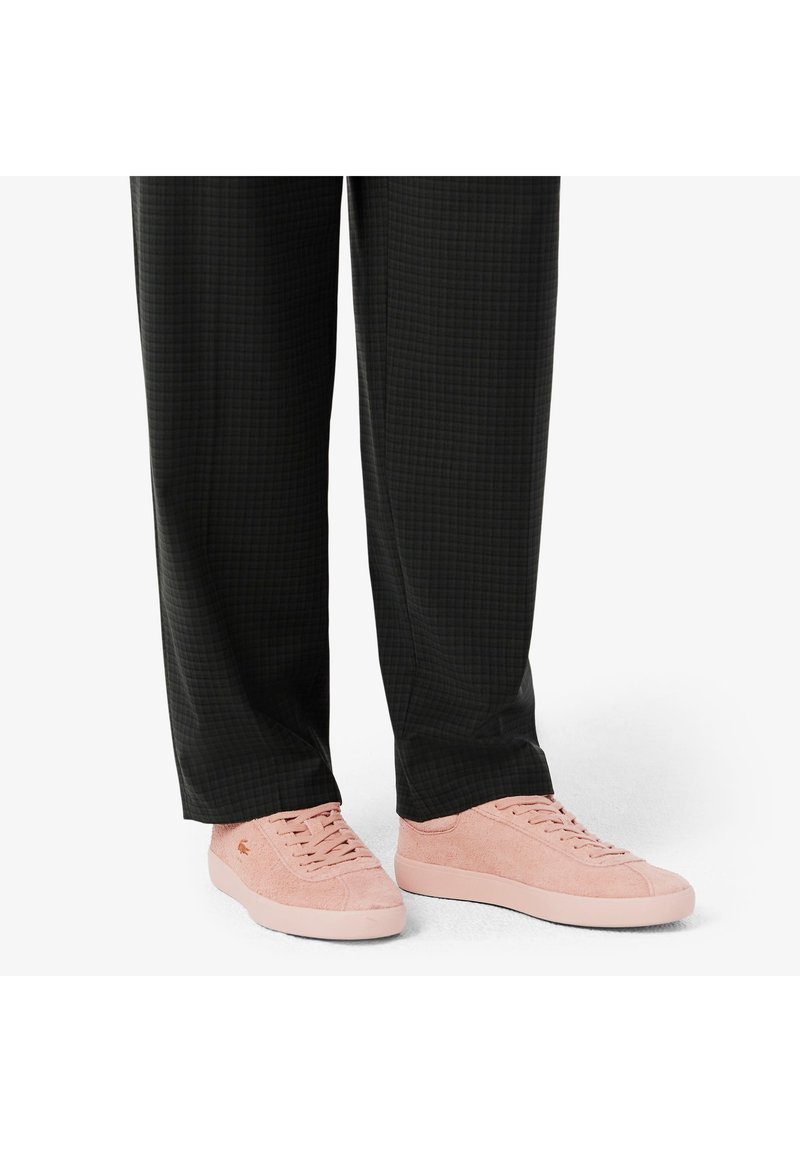 Sneakers texturizzati rosa chiaro con profilo basso, caratterizzati da una suola piatta e design con lacci, abbinati a pantaloni a scacchi neri.