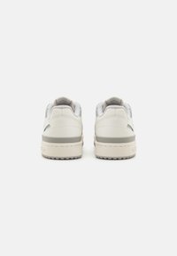 Vita lädersneakers med grå detaljer och texturerad yta, med platt sula, vadderad krage och minimalistisk design.