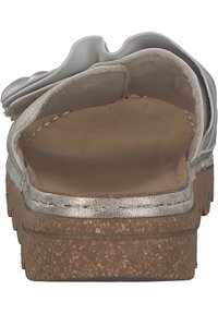 White slide sandal with silver metallic accents and a soft fabric ruffle. Cork sole with a textured finish and cushioned interior.