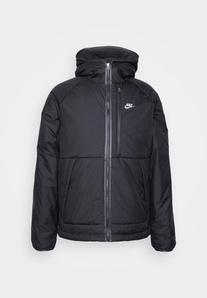 Zwarte gewatteerde jas met capuchon, voorzien van een volledige rits aan de voorkant, elastische manchetten en een Nike-logo aan de bovenkant aan de linkerkant. Soepele textuur.
