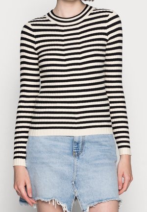 Pull en côtes à rayures noir et blanc avec un col rond, des manches longues et une coupe ajustée, associé à une jupe en denim bleu clair.