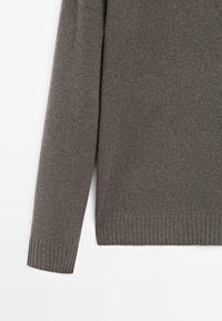 Langärmeliger grauer Strickpullover mit gerippten Bündchen und Saum, auf weißem Hintergrund präsentiert.
