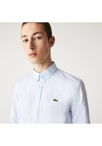 Light blue button-up shirt made of cotton with a collar, featuring a small green embroidered crocodile logo on the left chest.