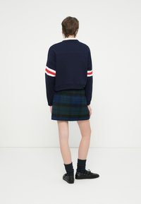 Sudadera corta en navy con mangas a rayas rojas y blancas, combinada con una mini falda de cuadros verde, calcetas negras y zapatos negros.