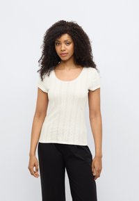 Κρεμ τοπ με κοντά μανίκια και στρογγυλή λαιμόκοψη, με κάθετα υφασμάτινα σχέδια και κυματιστό τελείωμα. Συνδυάζεται με μαύρο, άνετο παντελόνι.