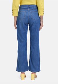 Wijd-benige jeans in middelblauw denim; heeft twee achterzakken en een rafelige zoom. Gepaard met gele blokhakken sandalen.