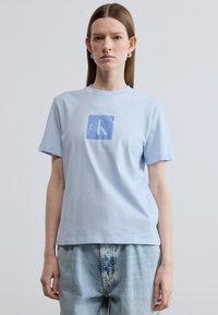 Ανοιχτό μπλε βαμβακερό t-shirt με κοντά μανίκια, με τετράγωνο γραφικό λογότυπο σε πιο σκούρο μπλε στο κέντρο. Μαλακή υφή, άνετη εφαρμογή.