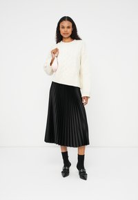 Suéter blanco de punto trenzado, falda midi plisada negra, calcetines negros hasta el tobillo, zapatos negros de punta; sosteniendo un bolso de mano rosa pálido.