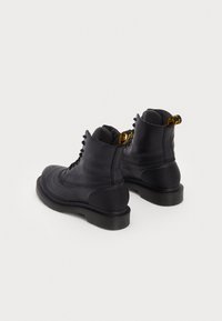 Botine din piele neagră până la gleznă, cu vârf rotund, suprafață texturată, talpă din cauciuc negru și fereastră galbenă la spate. Design cu șireturi.