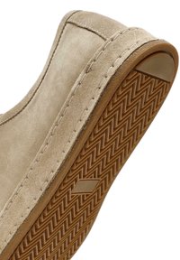 Zapato de ante beige con suela de goma texturizada que presenta un patrón de espiga. Las costuras laterales añaden detalle al diseño superior.