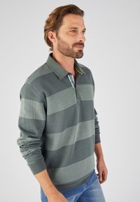 Groen en grijs gestreepte polo met een kraag en knoopsluiting. Beschikt over een textuurstof met een geel en blauwe accent onder de kraag.