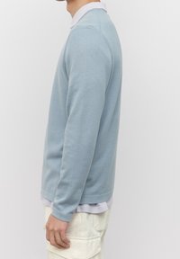 Maglione lavorato a maglia di colore azzurro chiaro con scollatura a girocollo e maniche lunghe. Presenta un bordo inferiore e polsini a coste, indossato sopra una camicia grigia chiara.
