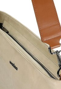 Borsa a tracolla in pelle color crema con tracolla regolabile marrone chiaro, cerniera argento e marchio discreto. Texture liscia con design minimalista.