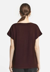 Burgundy t-shirt med kort ärm, avslappnad passform, bred halsringning och mjukt tyg. Sømlös bakdel med en slät textur och enkel design.