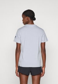 Hellgraues Baumwoll-T-Shirt mit kurzen Ärmeln und rundem Halsausschnitt. Verfügt über ein blaues Logo auf dem linken Ärmel und eine glatte Textur.