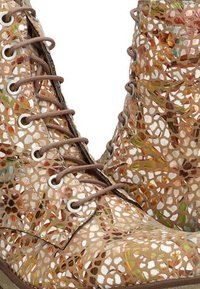 Botas de tobillo con cordones en un patrón de mosaico que presenta tonos beige, marrón y verde, elaboradas con cuero texturizado y ojales plateados.