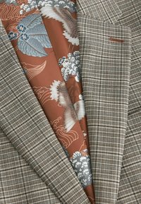 Graham kariertes Blazer mit einer strukturierten Stoff; verfügt über ein braunes Blumenfutter mit blauen und weißen Akzenten, die komplexe Muster hervorheben.