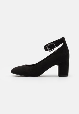 Sort ruskinds ankelstropp pump med spids tå og blokhæl. Har en sølv spænde for justerbar pasform. Glat tekstur.