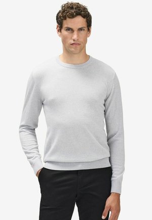 Lys grå crew-neck sweater lavet af blødt strikket stof. Har lange ærmer og en ribbet kant. Sammen med mørke bukser.