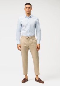 Hellblau gestreifte Button-Down-Bluse, beigen Hosen mit Kordelzug, braune Slipper; glattes Material, taillierte Form und subtile Texturen.