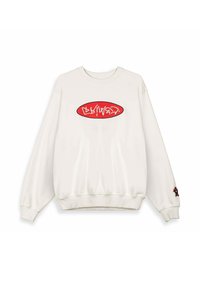 Sudadera blanca de cuello redondo con un logo ovalado rojo que presenta texto estilizado en blanco en el pecho y un pequeño oso de peluche bordado en el puño de la manga derecha.
