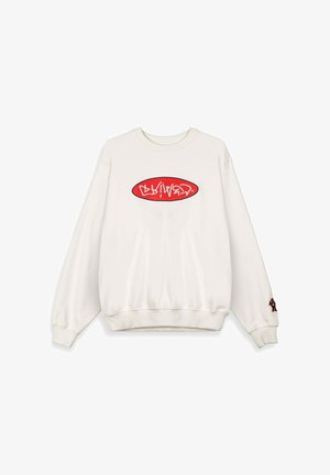 Sudadera blanca de cuello redondo con un logo ovalado rojo que presenta texto estilizado en blanco en el pecho y un pequeño oso de peluche bordado en el puño de la manga derecha.