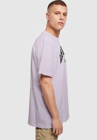 Lilla bomulds t-shirt med korte ærmer, med sort tekstlogo på forsiden. Afslappet pasform, rund halsåbning, glat tekstur.