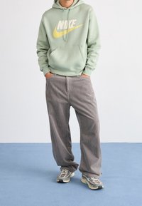 Mintgrön huvtröja med en gul Nike-logga, tillsammans med grå kordflätsbyxor med vida ben och grå sneakers med multicolorerade detaljer.