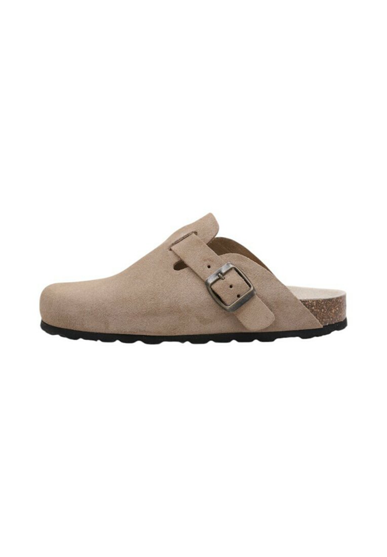 Sabots en suédine beige avec un design courbé, détail de boucle sur le côté et semelle en liège, dotés d'une semelle en caoutchouc noir texturé.